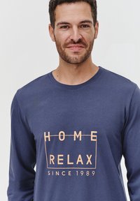 Granatowa koszula z długim rękawem, wykonana z miękkiego materiału, z pomarańczowym napisem: "HOME RELAX" oraz "SINCE 1989" w wyraźnej czcionce.