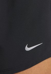 Juodos sportinės šortai, pagaminti iš lygios, lengvos medžiagos, su sidabriniu Nike logotipu apatinėje pusėje ir plokščiomis siūlėmis.