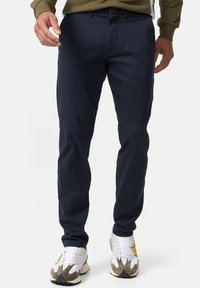 Chinos navy en coton, avec une coupe droite, fermeture à bouton et poches latérales. Portés avec des baskets blanches et taupes.