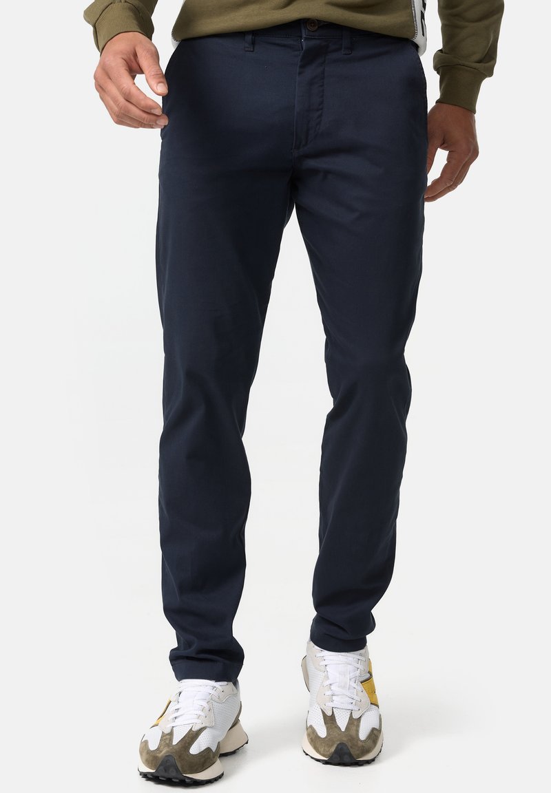 Chinos navy en coton, avec une coupe droite, fermeture à bouton et poches latérales. Portés avec des baskets blanches et taupes.