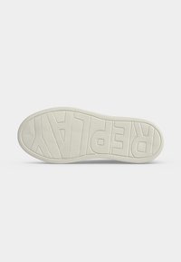 Semelle d'une sneaker de couleur claire avec le mot "REPLAY" embossé en bas, sur fond blanc uni.