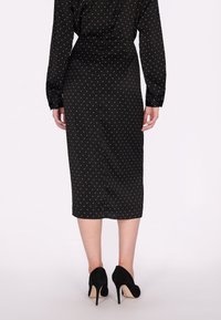 Musta mekko, jossa valkoisia pilkkuja, pitkät hihat, taipuva siluetti, polvipituinen, yhdistetty mustiin korkokenkiin. Sujuvuus kangasrakenteessa.