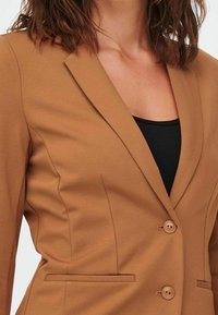 Blazer marron sur mesure avec une fermeture à un bouton, deux poches avant et une texture lisse. Dispose d'un col classique et d'un design élégant.