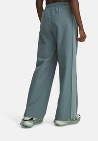 Light teal wide-leg trousers with an elastic waistband and black side stripes, paired with sleek green sneakers featuring mesh details.
