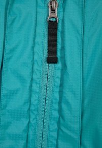 Tyrkysová bunda na zip s hladkým povrchem, vybavená kovovým zipem a černým nylonovým táhlem podél předního švu.