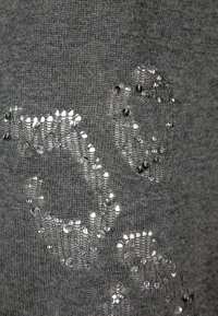 Grau gestrickter Stoff mit glänzenden silbernen Pailletten, die in einem Muster angeordnet sind und eine strukturierte Details auf der Oberfläche erzeugen.