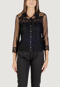 Blusa nera con maniche trasparenti a pois, dettagli in pizzo e chiusura frontale con bottoni color oro. Design strutturato e alla moda.