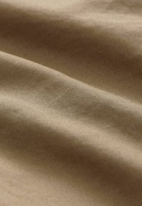 Strukturiertem Stoff in einem warmen Beigeton, der sanfte, glatte Falten und eine matte Oberfläche zeigt, mit subtilen Variationen in der Farbintensität.