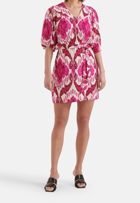 Kortärmad knälång klänning i rosa och krämfärgad ikatmönster, med bälte i midjan och v-ringning. Bärs med svarta klacksandaler.