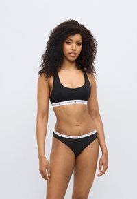 Μαύρο αθλητικό σουτιέν και ταιριαστά μαγιό κάτω μέρος από λείο ύφασμα. Το σουτιέν διαθέτει λευκή λωρίδα με λογότυπο και κόκκινες λεπτομέρειες. Απλός σχεδιασμός.