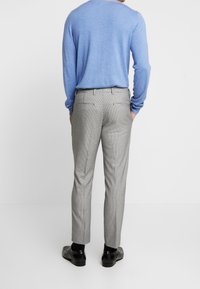 Maglione blu chiaro a maglia e pantaloni grigi a quadri con vestibilità slim; i pantaloni hanno due tasche sul retro e scarpe nere.