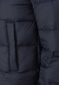 Primo piano di tessuto imbottito trapuntato di giacca a piumino blu navy con tasca visibile e dettagli di cuciture imbottite.