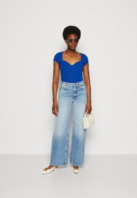 Blue ribbed bodysuit with a sweetheart neckline, paired with high-waisted, wide-leg light blue jeans, and white slip-on shoes.