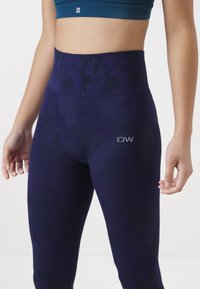 Hoggewaisted paarse legging met een gestructureerd oppervlak, voorzien van een subtiel patroon en een klein zilveren logo aan de zijkant. Rekbare stof.