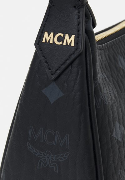 Schwarze Ledertasche mit strukturierter Oberfläche, die subtile MCM-Logo-Muster und einen goldfarbenen Logo-Anhänger am Trageriemen aufweist.