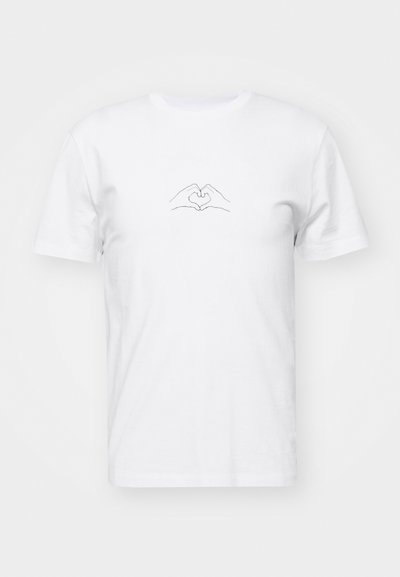 Camiseta de algodón blanca con un dibujo minimalista en línea negra de dos manos formando una figura de corazón en el centro frontal.