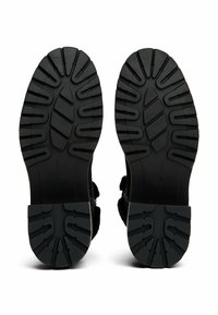 Semelle extérieure en caoutchouc noir avec des rainures profondes pour une meilleure traction, présentant une texture lisse et des bords arrondis. Conçue pour l'adhérence et la durabilité.