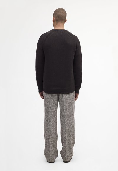 Zwarte, gestructureerde gebreide trui met raglanmouwen; gecombineerd met lichtgrijze, wijde broek met een gespikkeld patroon.