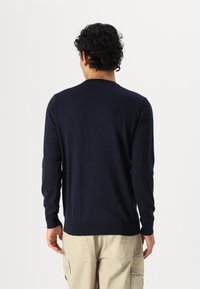 Μαύρο μπλουζάκι με μακριά μανίκια κατασκευασμένο από απαλό ύφασμα με στρογγυλή λαιμόκοψη και ριμπ μανσέτες, συνδυασμένο με ανοιχτόχρωμο παντελόνι cargo.