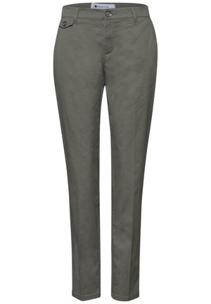 Gros plan de la main d'une personne dans la poche avant d'un pantalon vert olive avec une poche à rabat boutonnée et des coutures visibles.