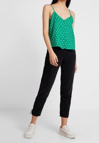 Camisola verde a pois con spalline sottili e apertura con bottoni, abbinata a jeans neri cropped e sneakers bianche.