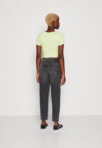 Limonkowa krótka koszulka z falbaniastym dołem w zestawieniu z czarnymi jeansami o wysokim stanie i czarnymi butami wsuwanymi. Prosta, codzienna stylizacja.