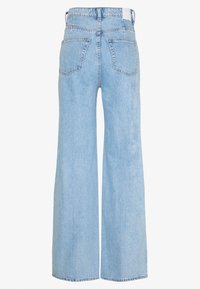 Jean en denim bleu clair avec une coupe large, doté d'une taille haute, de cinq poches et de coutures visibles le long des coutures.