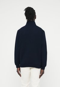 Μπλε σκούρο φούτερ με ψηλό γιακά, μανσέτες και τελείωμα με ριμπ, με υφή στο ύφασμα και λεπτομέρεια αερισμού στο πίσω μέρος.