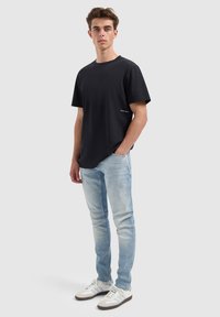 Zwarte katoenen T-shirt met korte mouwen en een ronde halslijn, gecombineerd met lichtblauwe denim jeans en witte sneakers met grijze accenten.