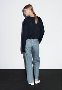 Marinblå kabelstickad tröja med långa ärmar, tillsammans med ljusblå raka jeans. Modellen har på sig vita slipskor som har en enkel design.