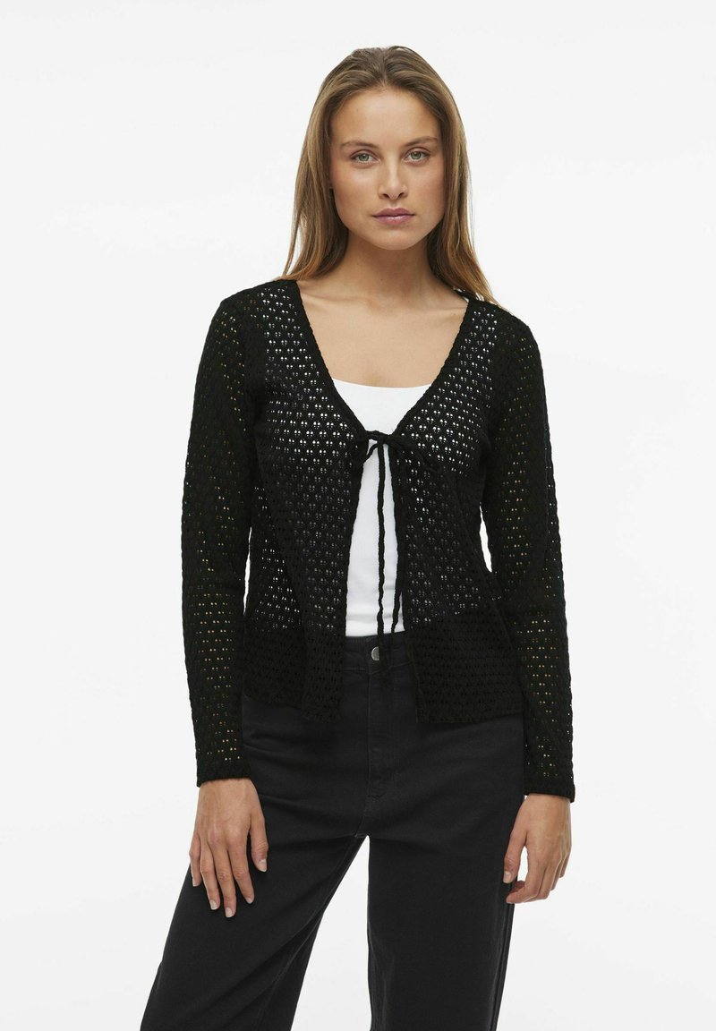 Cardigan nero in maglia con scollatura a V, chiusura con lacci nella parte anteriore, maniche lunghe e un motivo tessuto aperto e strutturato.