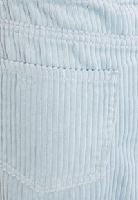 Hellblaues Cordstoffgewebe mit vertikaler Rippstruktur, einer auffälligen Gesäßtasche und kontrastierenden Nähdetails.