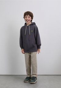 Gray hoodie with green accent logo, hood drawstrings, front pocket, paired with beige pants and teal shoes. Simple, casual outfit.