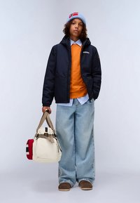 Marineblå boblejakke over en oransje genser, kombinert med lyseblå vide jeans. Beige veske med røde og blå detaljer. Strikkelue.