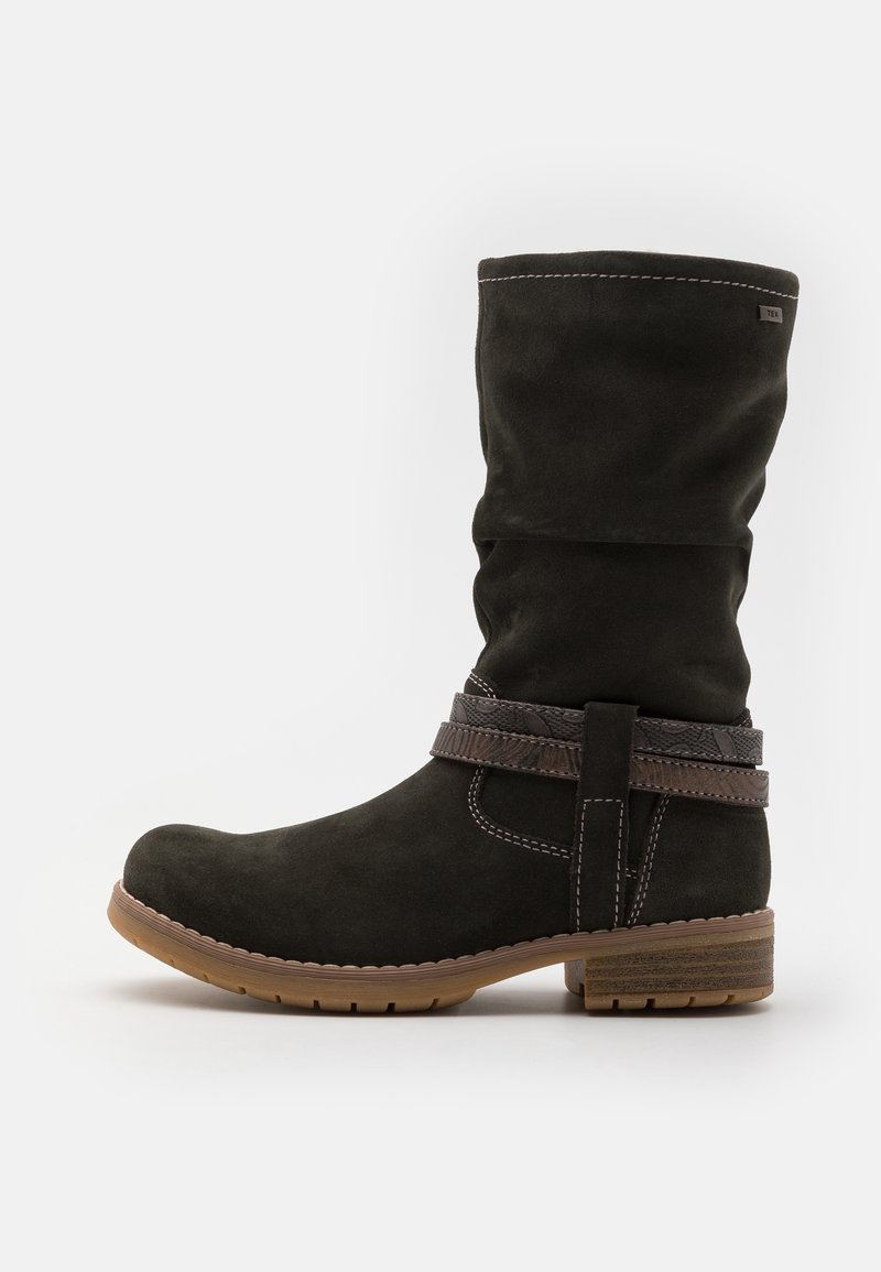 Bota de ante negra hasta la rodilla con una correa trenzada marrón, detalles de costura, puntera redondeada y suela de goma texturizada.
