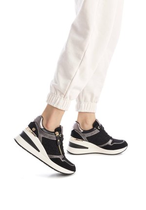 Zapatillas deportivas negras y plateadas con cierre de cremallera, acentos metálicos y paneles texturizados. Presentan un tacón cuña y suela de goma.