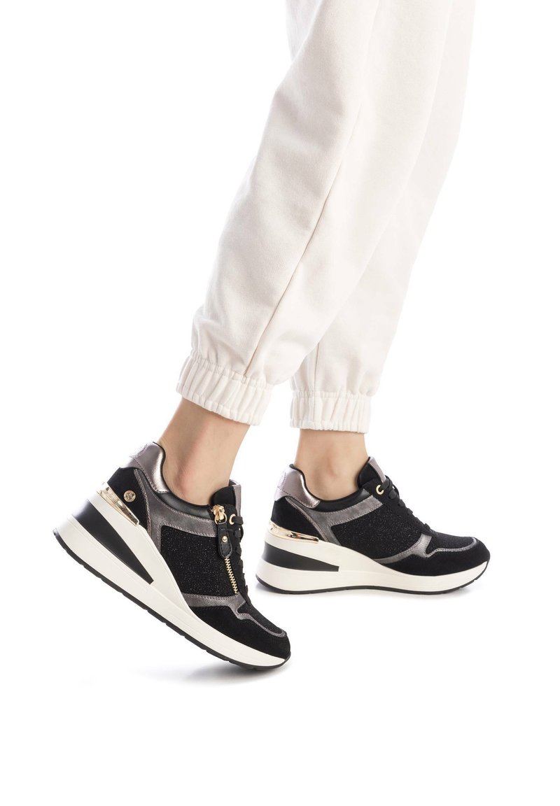 Scarpe sportive nere e argento con chiusura a zip, dettagli metallici e pannelli testurizzati. Presentano un tacco a zeppa e suola in gomma.