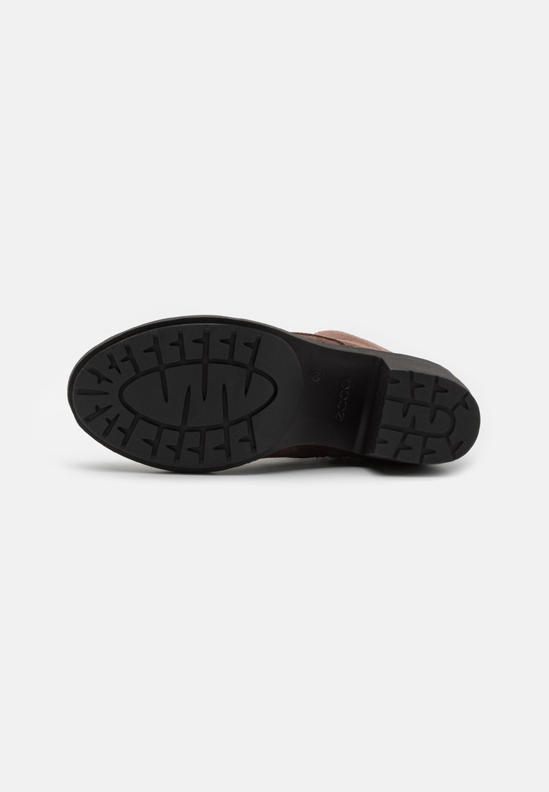 Braune Wildlederschuhe mit einer strukturierten schwarzen Gummisohle, die ein Profilmuster aufweist. Die Innensohle und der Absatz sind in einem dunkleren Braunton.