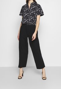 Camisa de botones de manga corta con estampado floral negro, combinada con pantalones sueltos negros. El conjunto se complementa con sandalias de tacón alto negras.