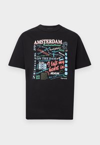 Schwarzes T-Shirt mit kurzen Ärmeln, bedruckt mit buntem, Amsterdam-themenbezogenem Text und Grafiken, darunter "Ich habe mein Herz gelassen in" und verschiedene Straßen- und Ortsnamen.