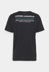 Svart bomull t-shirt med "UNDER ARMOUR" i vita bokstäver på baksidan, med ytterligare text ovanför i kontrasterande vitt och turkos.