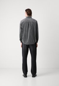 Striped long-sleeve shirt in gray and black with a button-down collar, paired with black pants. Soft texture with a relaxed fit.