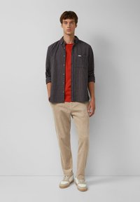 Lässiges Outfit mit einem dunkelkarierter Hemd, rotem T-Shirt, beigen Cordhosen und weißen Sneakern mit tanfarbenen Akzenten.