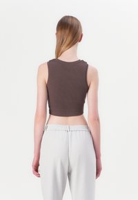 Cropped brown ribbed tank top with a round neckline, paired with light grey pants featuring an elastic waistband and relaxed fit.