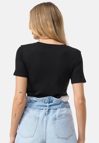 Černé žebrované tričko s krátkým rukávem a kulatým výstřihem, spojené s vysokým pasem světle modrými džíny, které mají výrazné zadní kapsy.