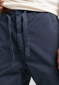 Pantalones de algodón azul marino con un acabado texturizado, que cuentan con una cintura con cordón, cierre de botón y bolsillos laterales.