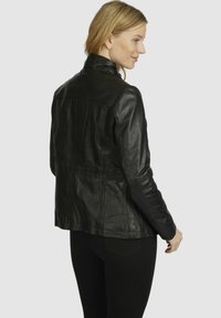 Black leather jacket with a fitted design, high collar, and visible stitching. Smooth texture and slightly shiny finish.