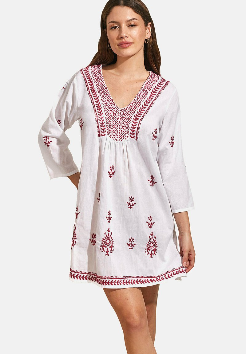 Robe blanche brodée avec un décolleté en V, des manches 3/4 et des motifs floraux rouges. Tissu léger avec un design ample et fluide.