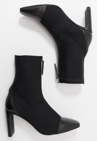 Bottines noires au design épuré, composées de tissu et de cuir, avec un bout pointu et un talon aiguille haut. Détail de fermeture éclair inclus.