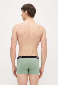 Cuecas boxer verde menta com cintura elástica preta exibindo o nome da marca "BOSS" em branco. Textura de tecido suave.